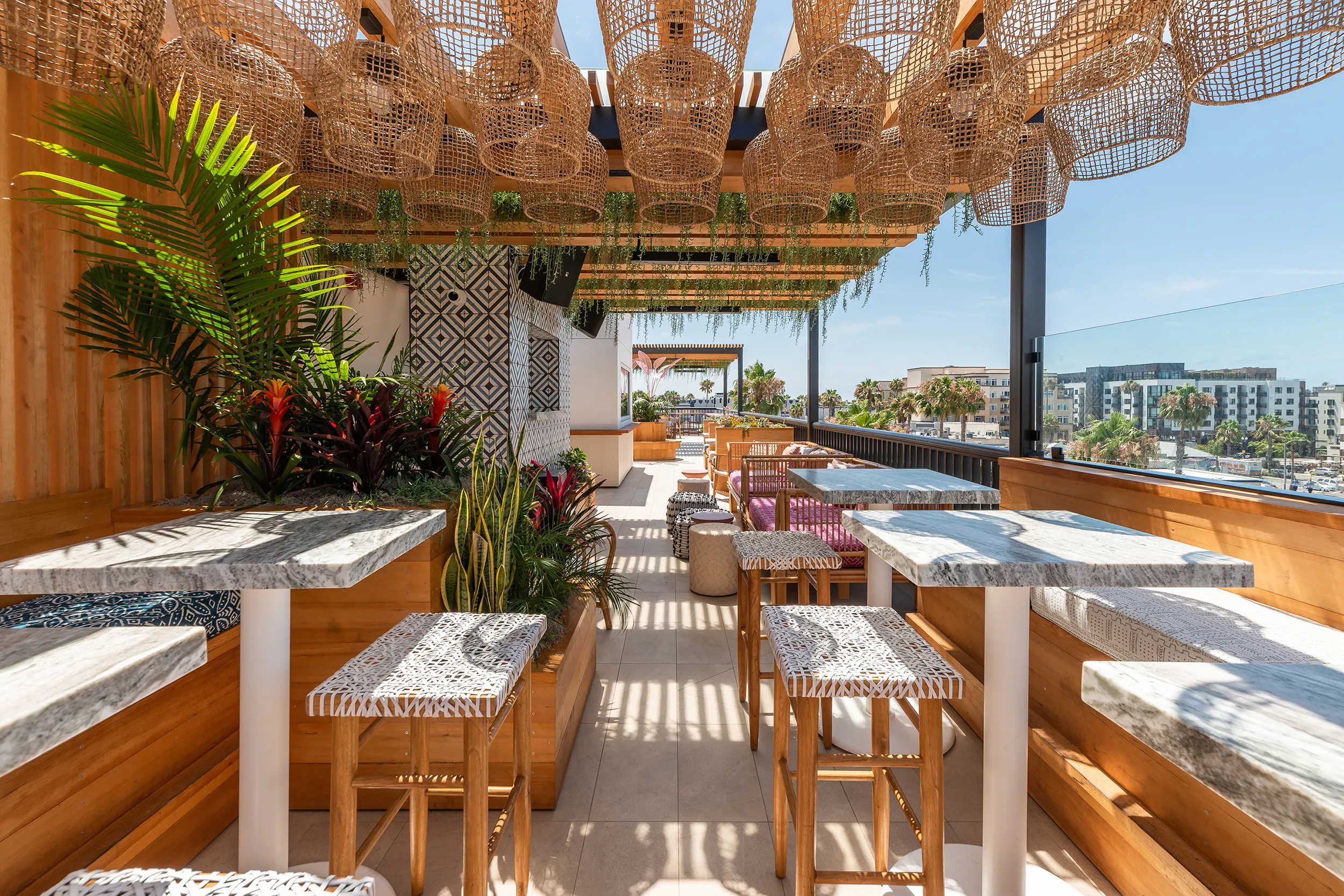 Cococabana rooftop dining area with rattan pendant lights, marble tables, tropical landscaping, and Downtown Oceanside views