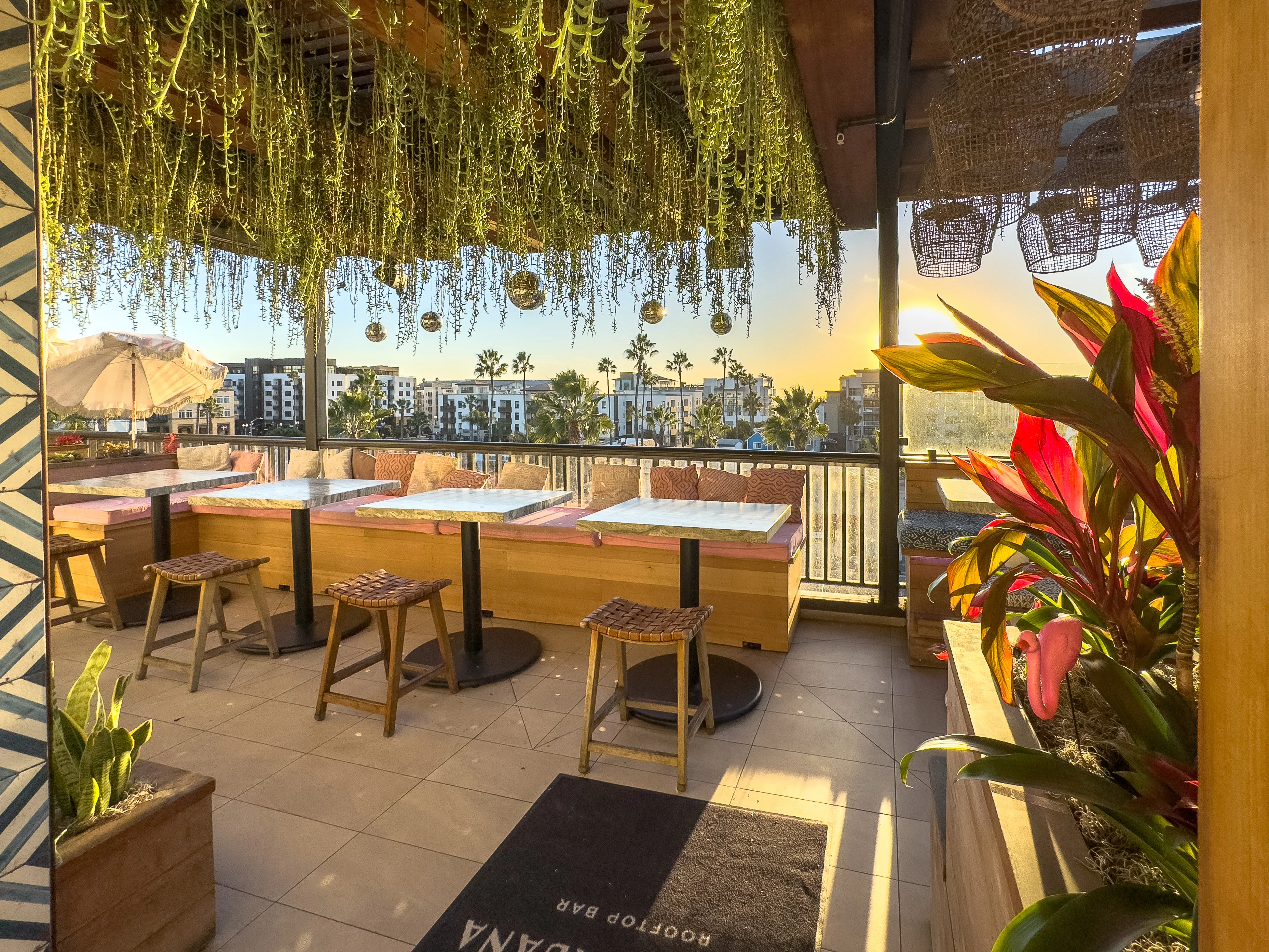 Coco Cabana rooftop lounge with pink daybeds, tile wall, and Oceanside city views at dusk