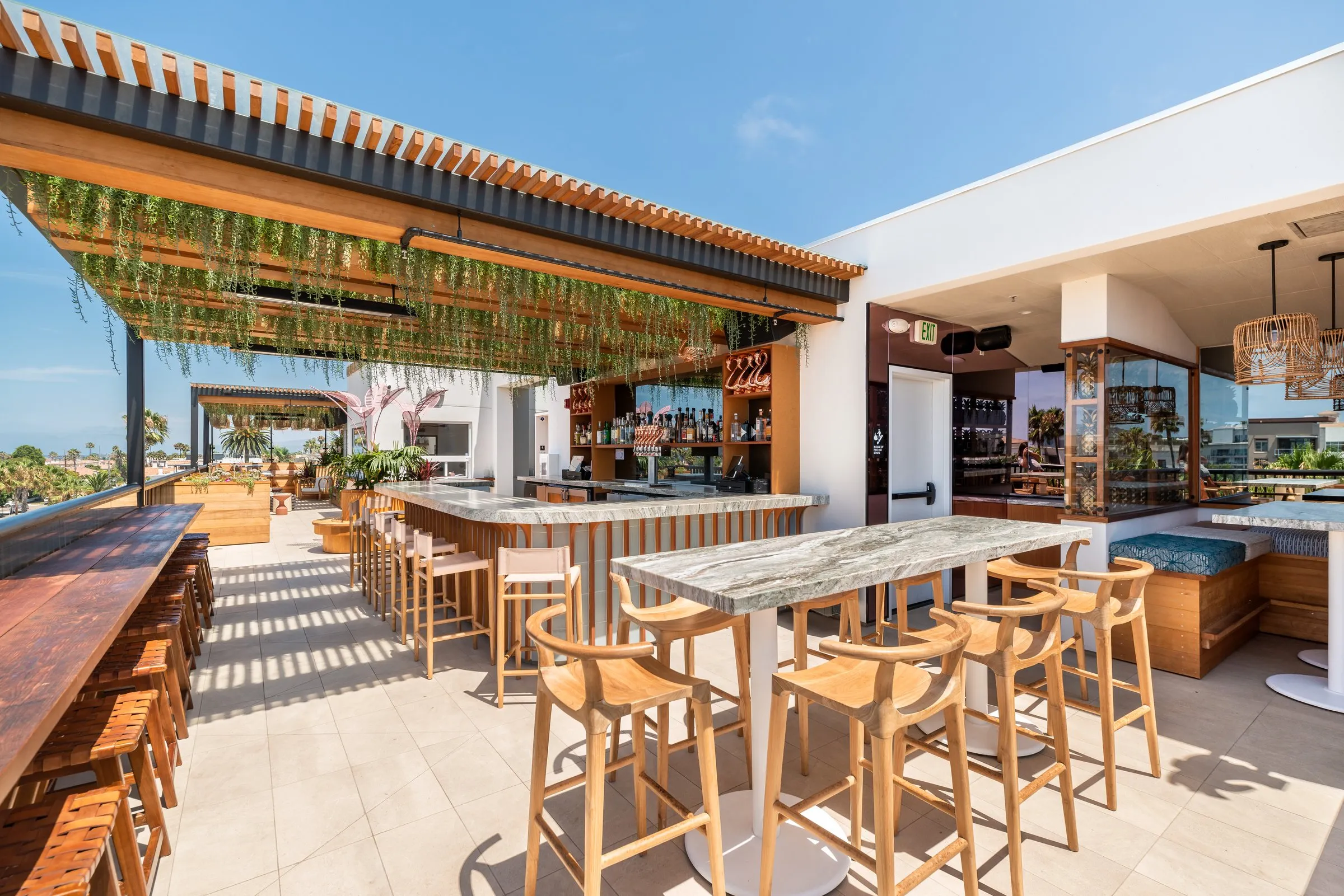 Cococabana open-air rooftop bar — marble counter, bar stools, hanging greenery, Oceanside views