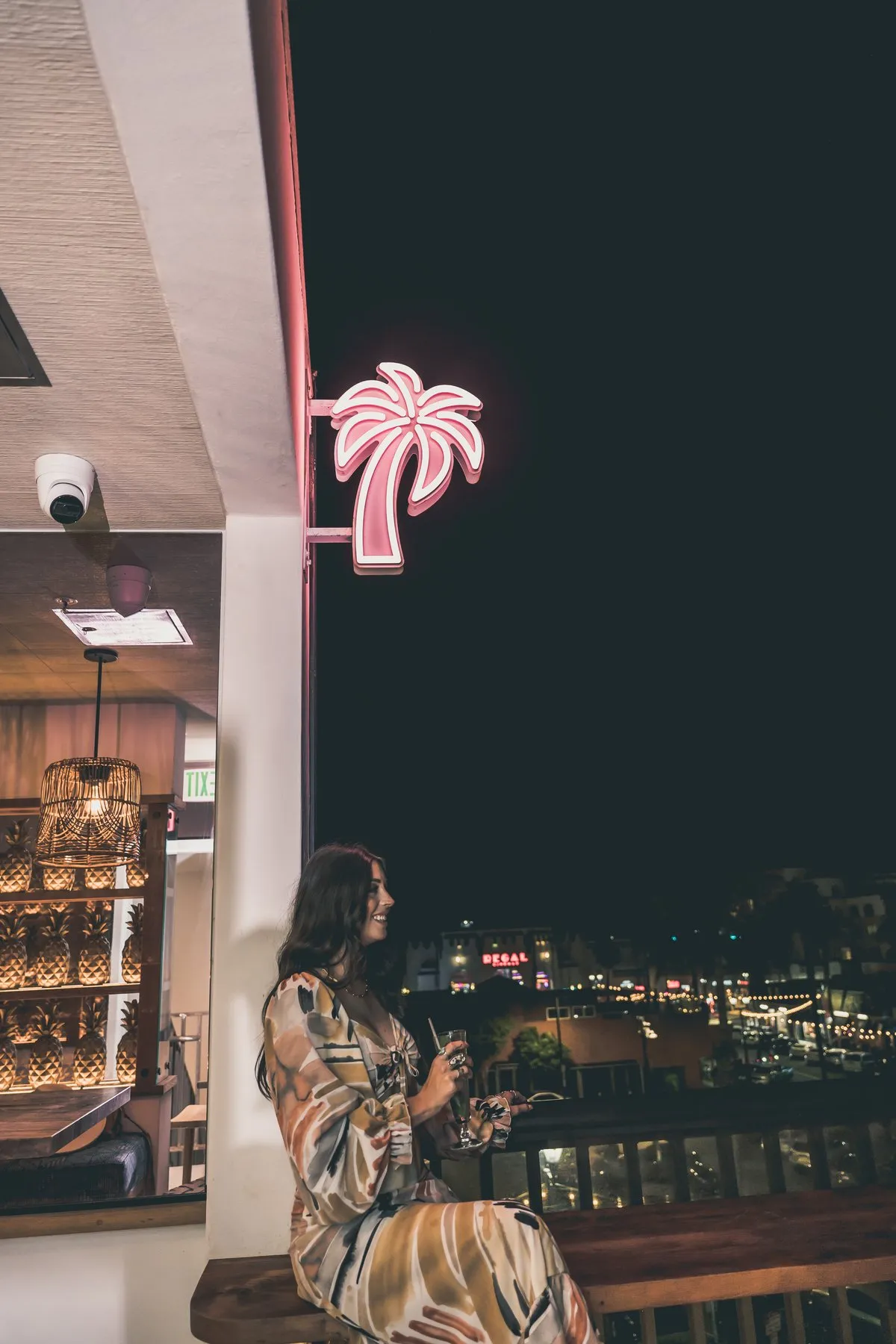 Neon pink palm tree sign glowing at Coco Cabana rooftop at night with guest below