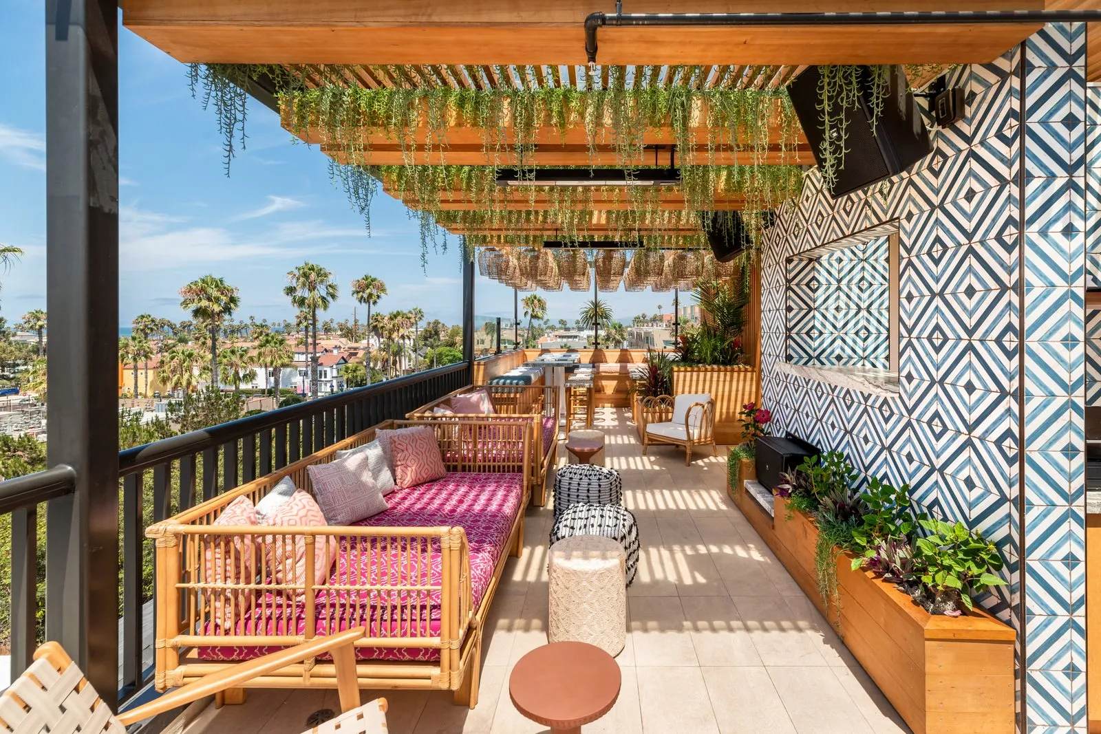 Coco Cabana rooftop lounge with pink daybeds, tile wall, and Oceanside city views at dusk